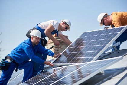 American jobs. Male team engineers installing stand-alone solar photovoltaic panel system. Electricians mounting blue solar module on roof of modern house. Alternative energy concept. Trina solar